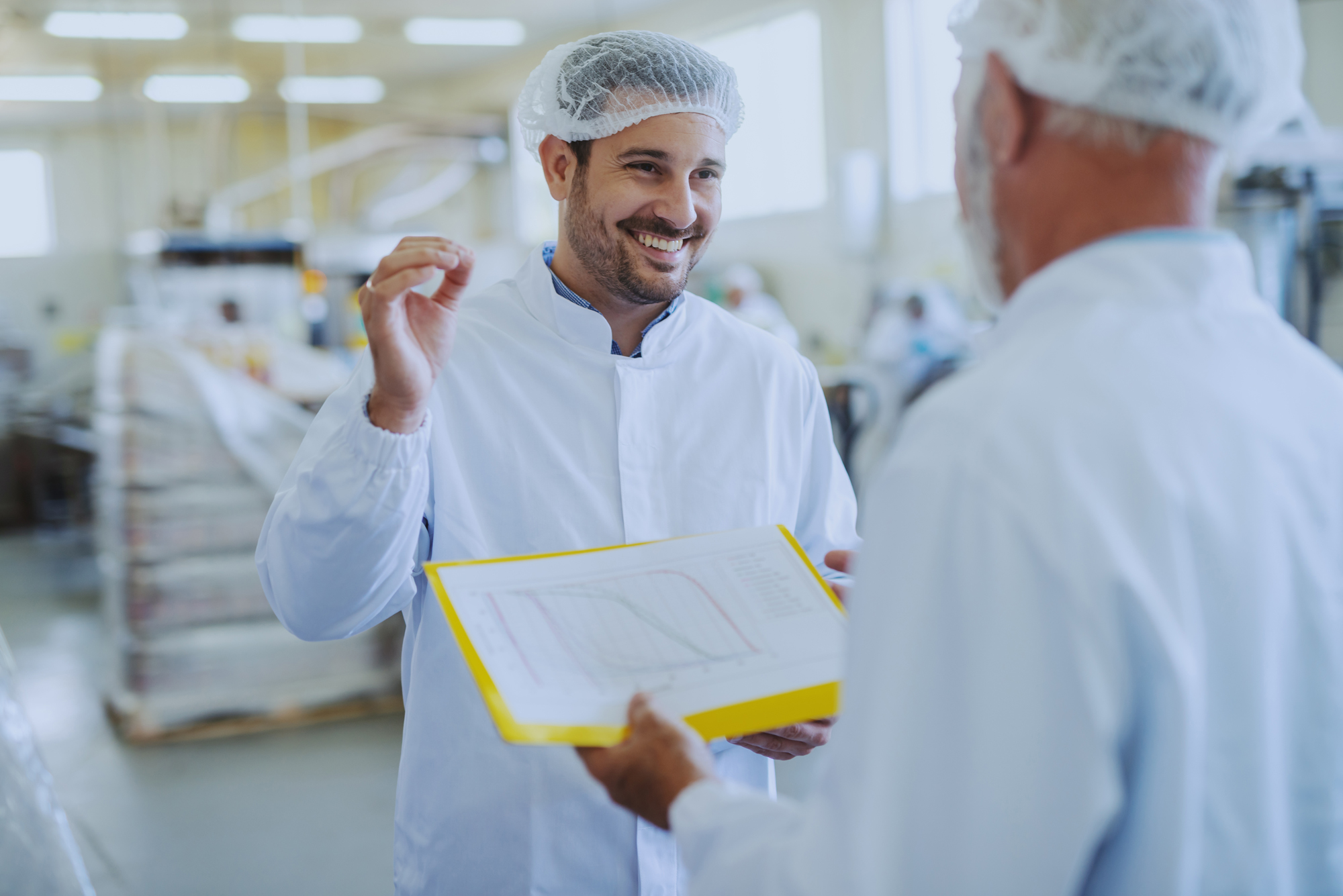 Smiling Food Safety Worker Discussing Safety Report with Another Worker
